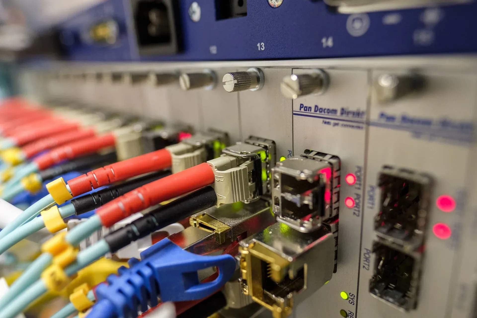 Fiber optic and Ethernet cables connected to a network patch panel with status lights