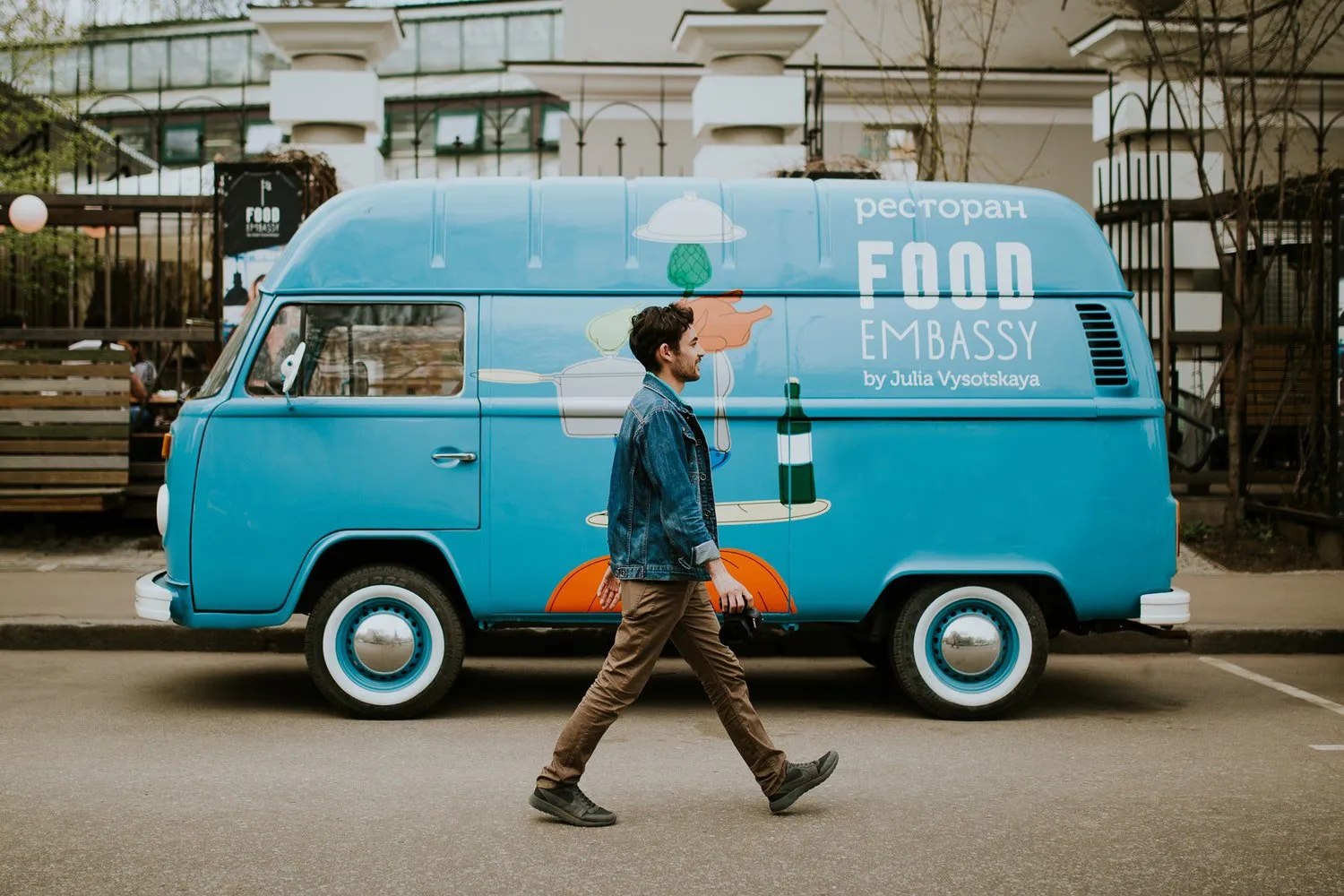 Man walking past a light blue food truck van on a city street