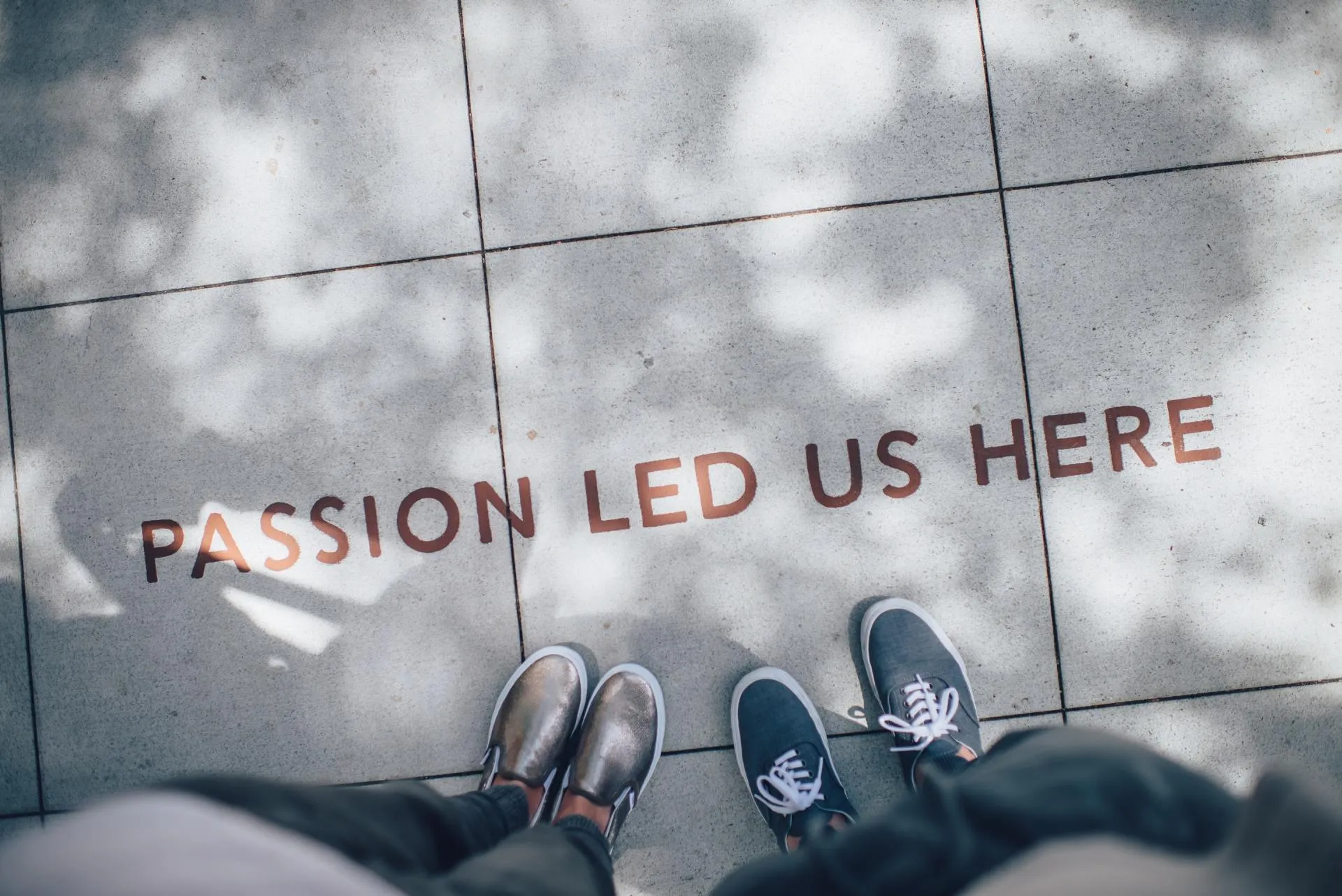 Two pairs of sneakers on a sidewalk painted with the words Passion Led Us Here