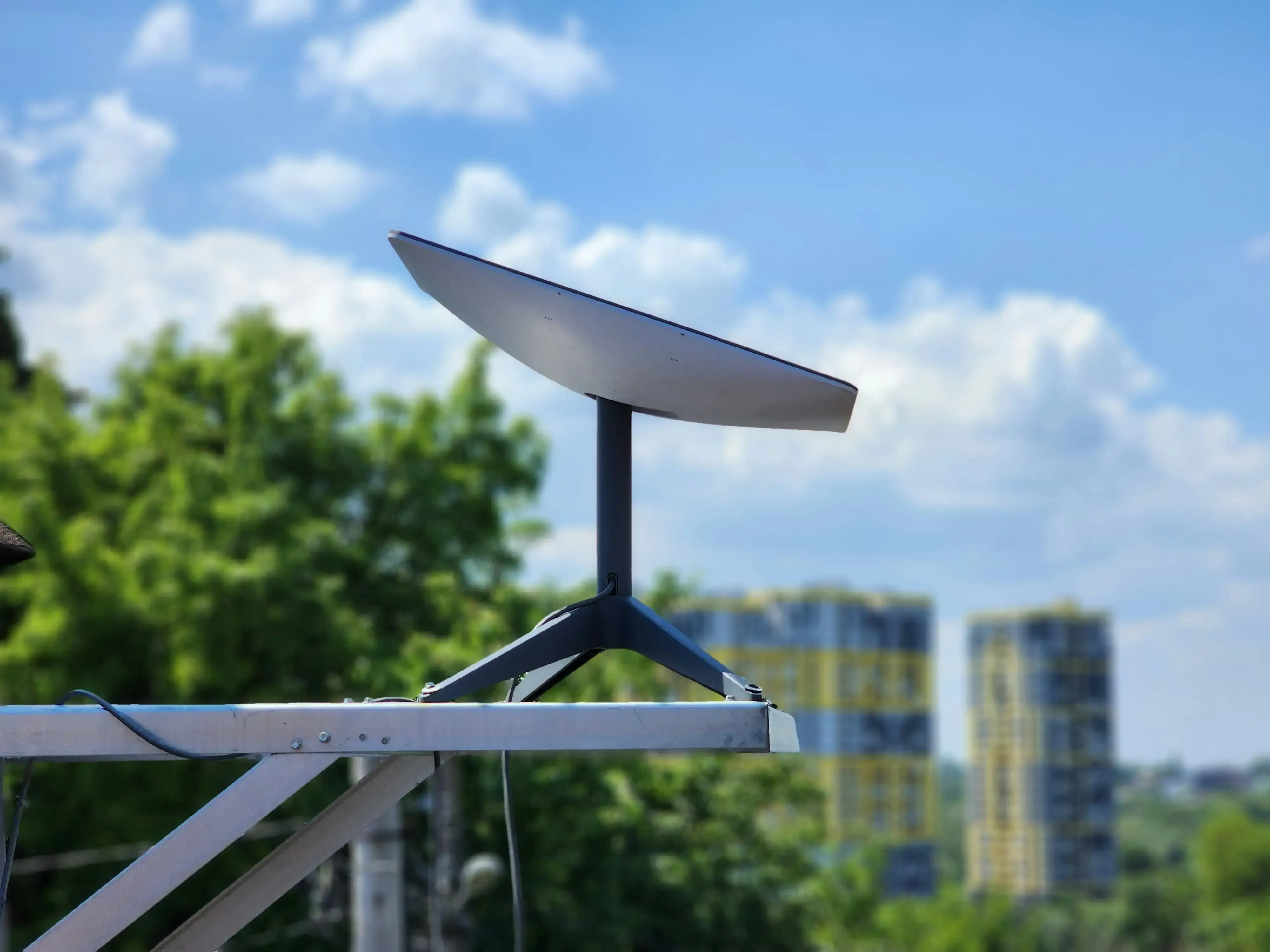 Starlink dish mounted on a rooftop railing with trees and city buildings behind