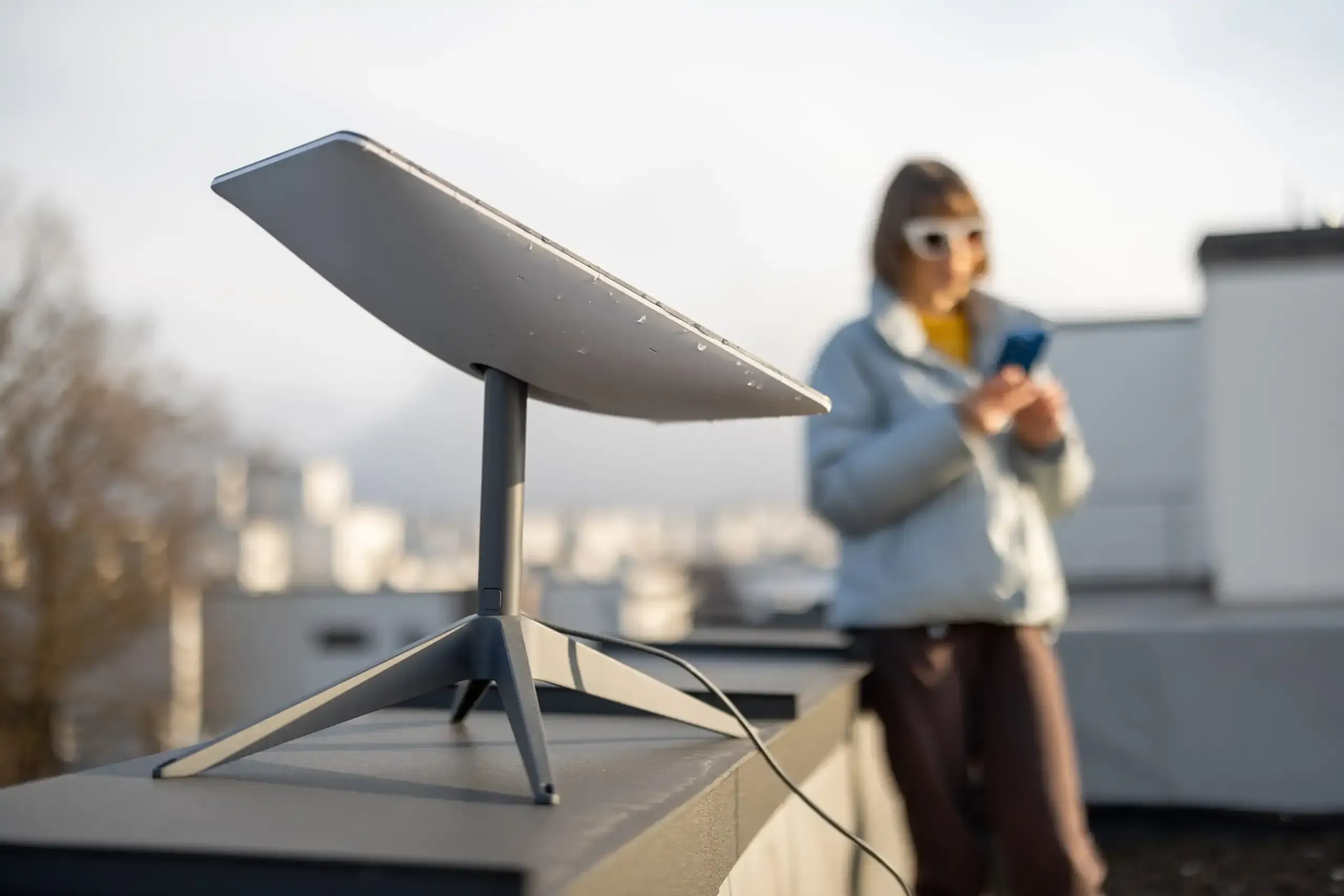 Starlink satellite dish on rooftop with person using phone.